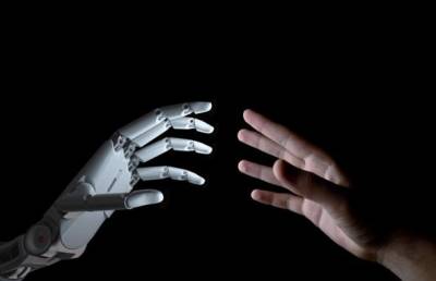 Close-up photo of raised robotic hand and human hand reaching toward each other about to touch.
