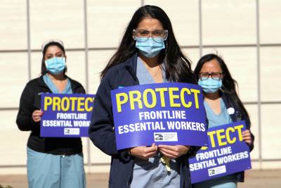 Image of health care workers wearing masks, and holding signs that say, 