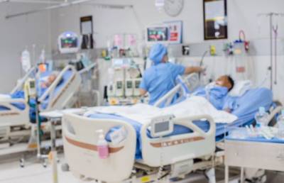Photo of two patients in ICU beds with health care provider working in between.