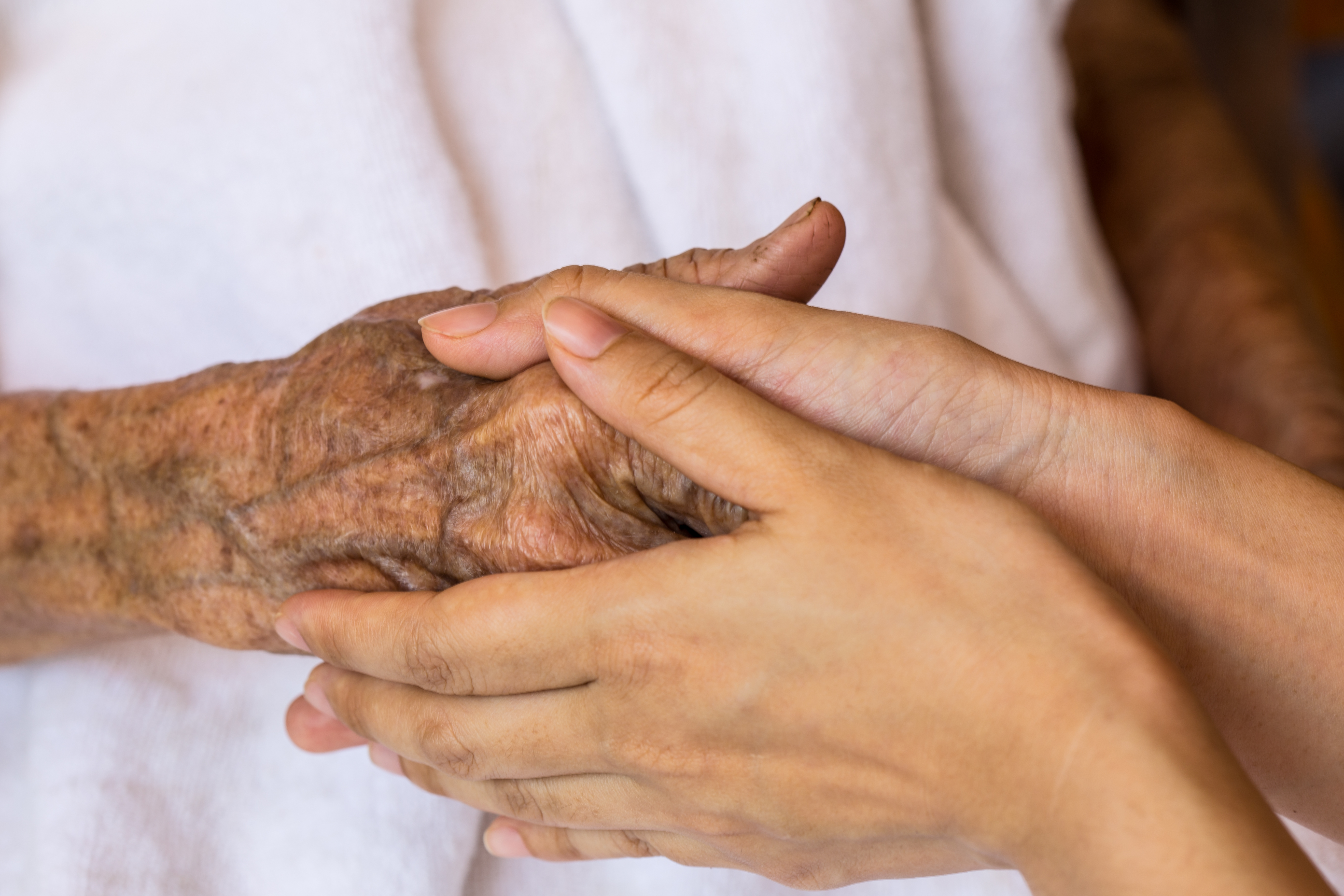 elderly person's hand clasped in young person's hands