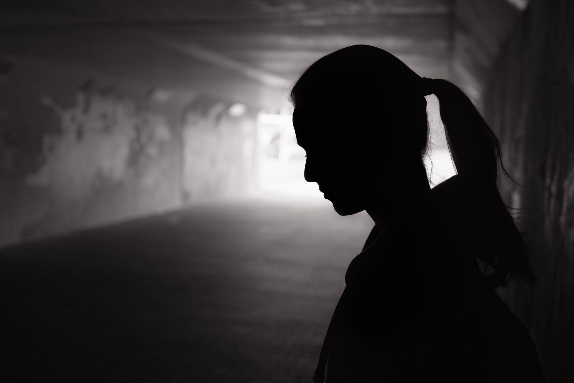 Black silhouette of girl with a pony tail looking down in a dark tunnel