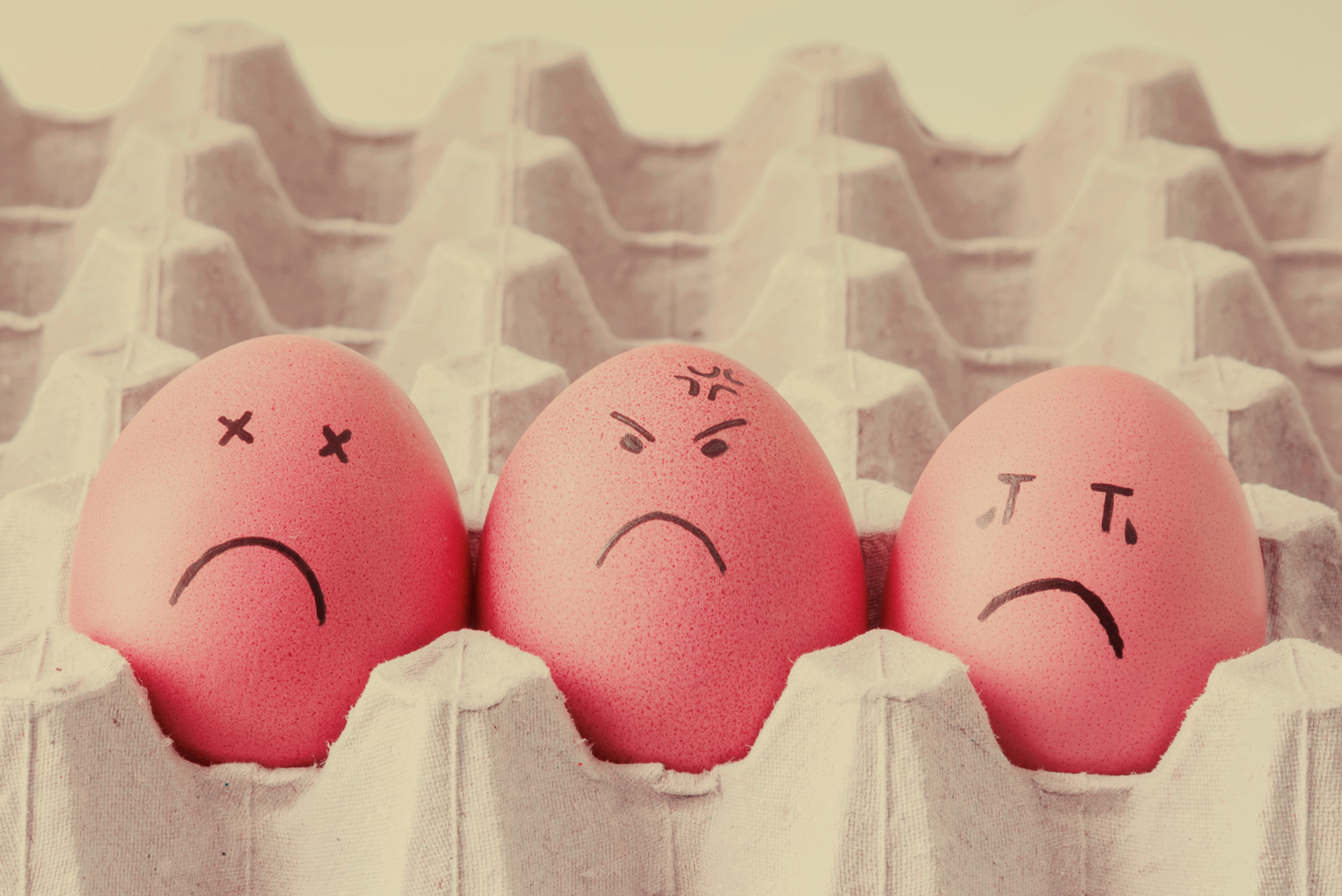 Three eggs in a carton with sad faces drawn on.