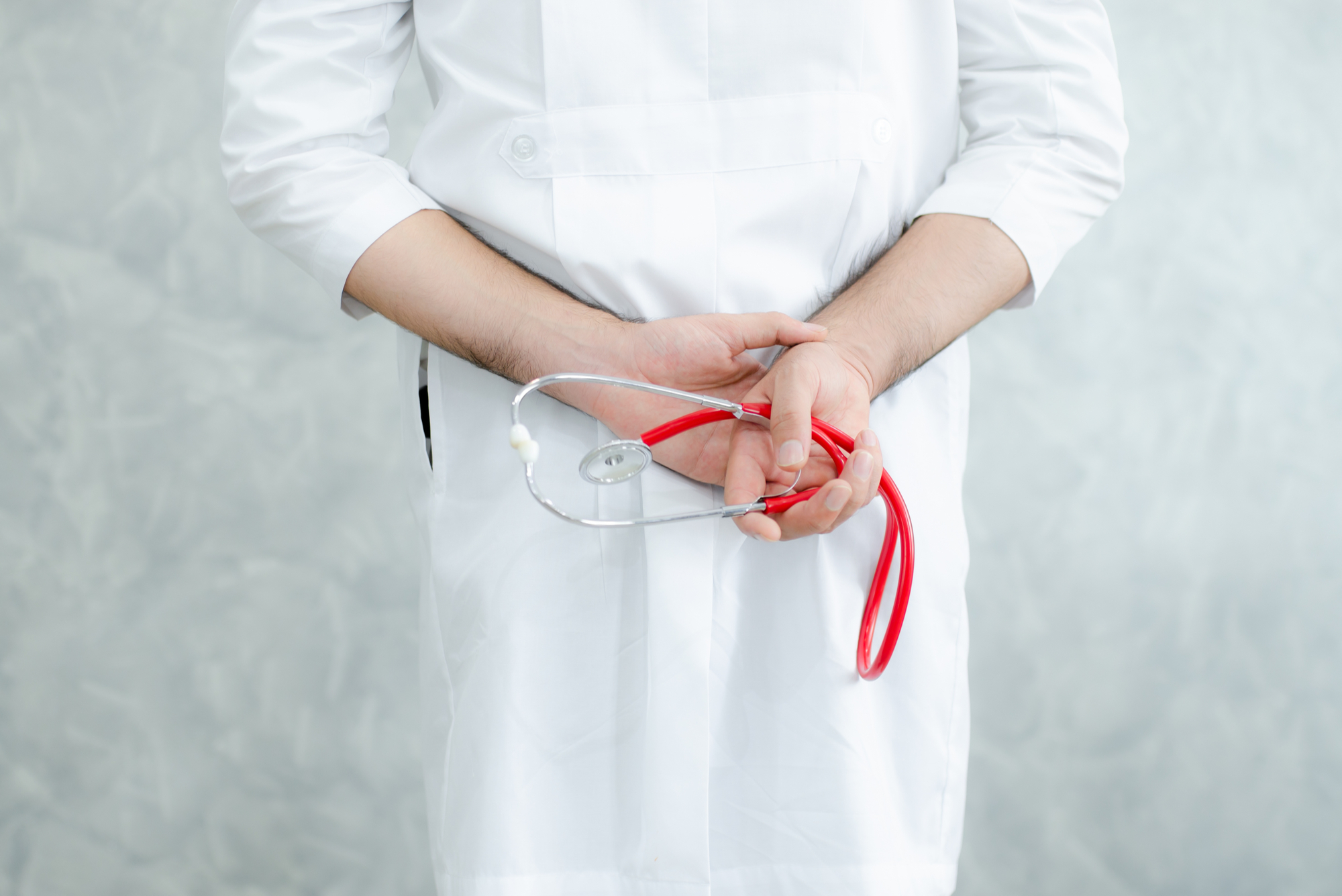 Back view of a doctor with his hands clasped behind his back holding a red stethoscope