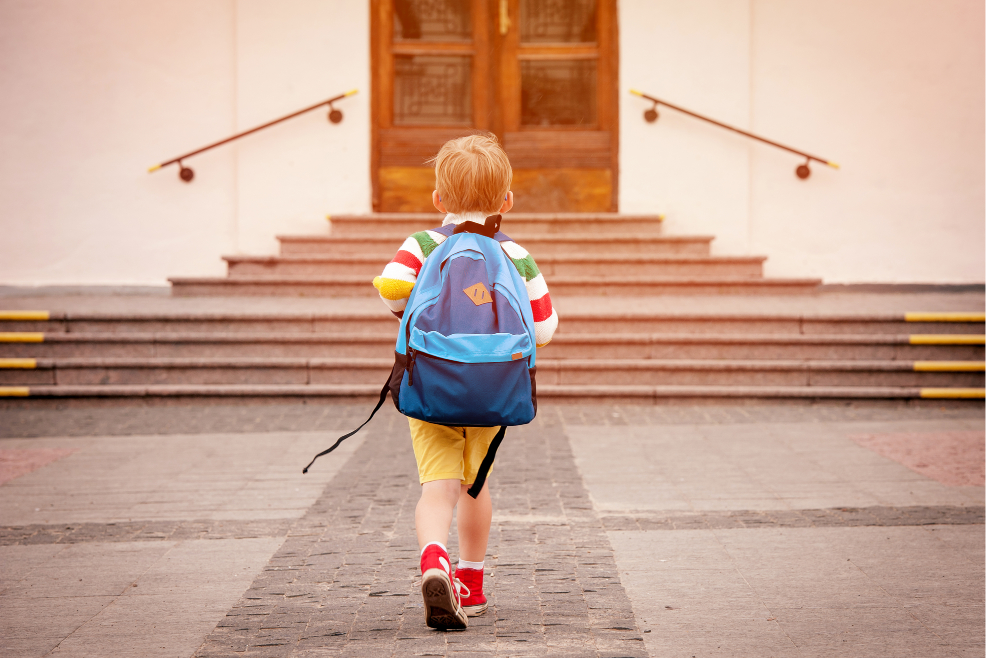 Back view of a little boy wearing a backpack walking to school