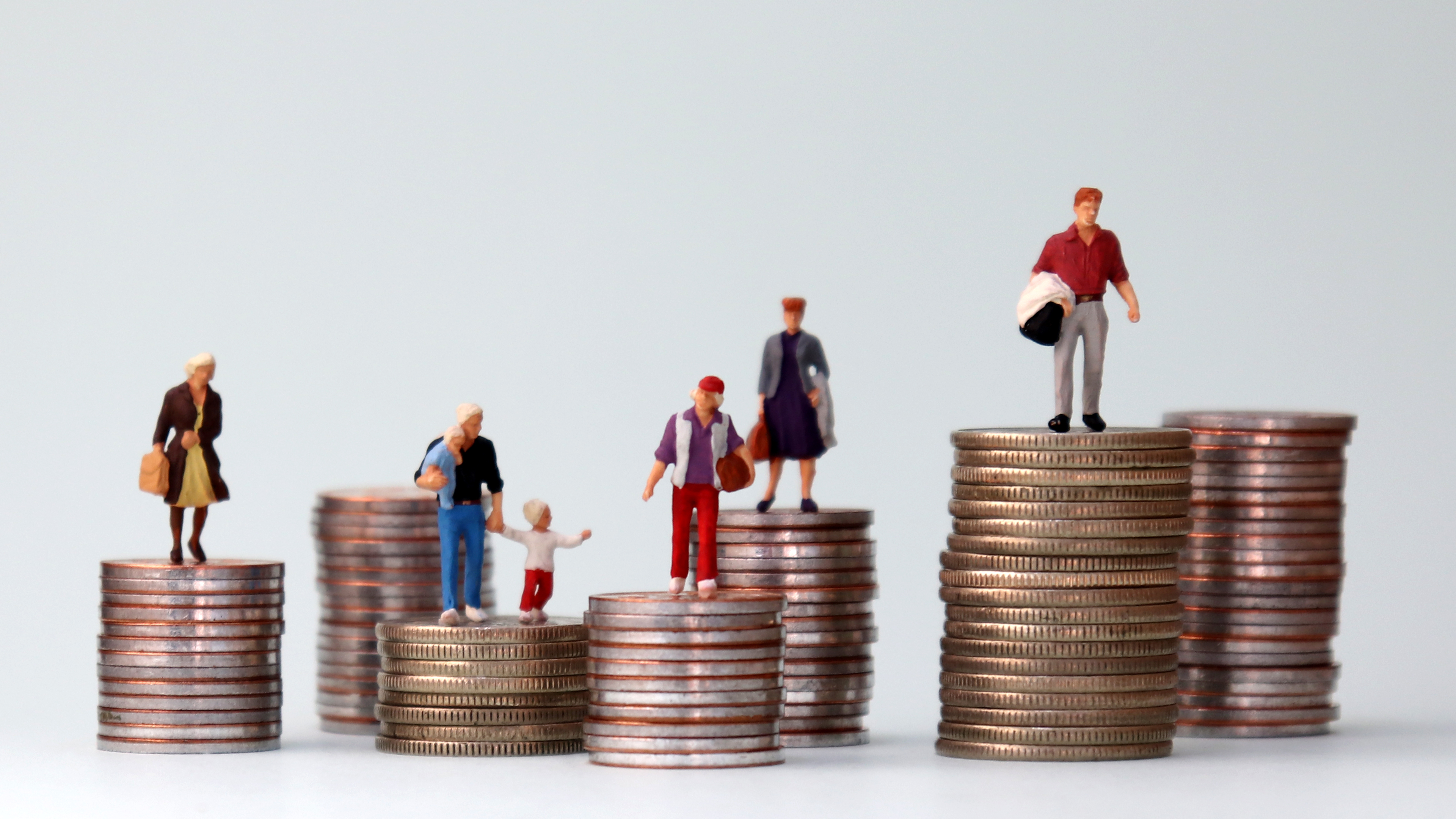 A photograph of miniature figures of people standing on top of piles of coins at different heights