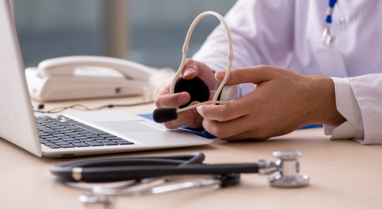 Photograph of a doctor holding a headset sitting in front of a laptop