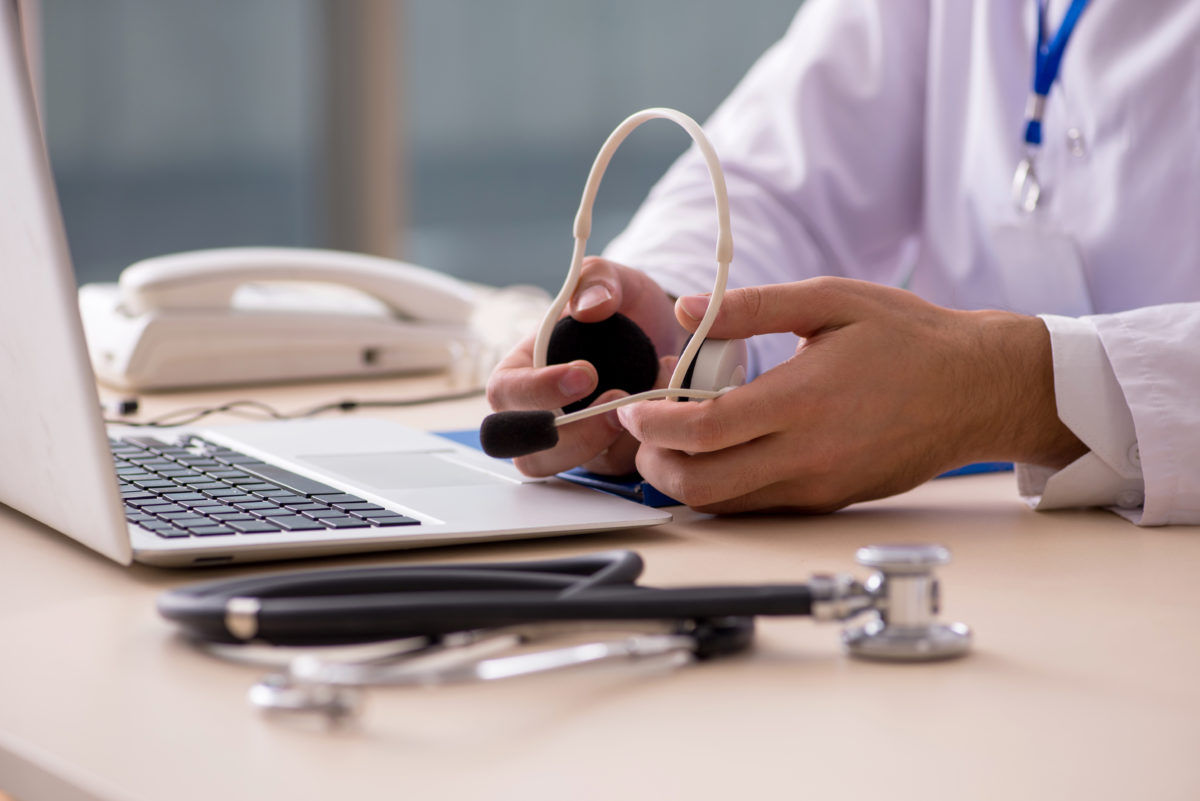 Photograph of a doctor holding a headset sitting in front of a laptop