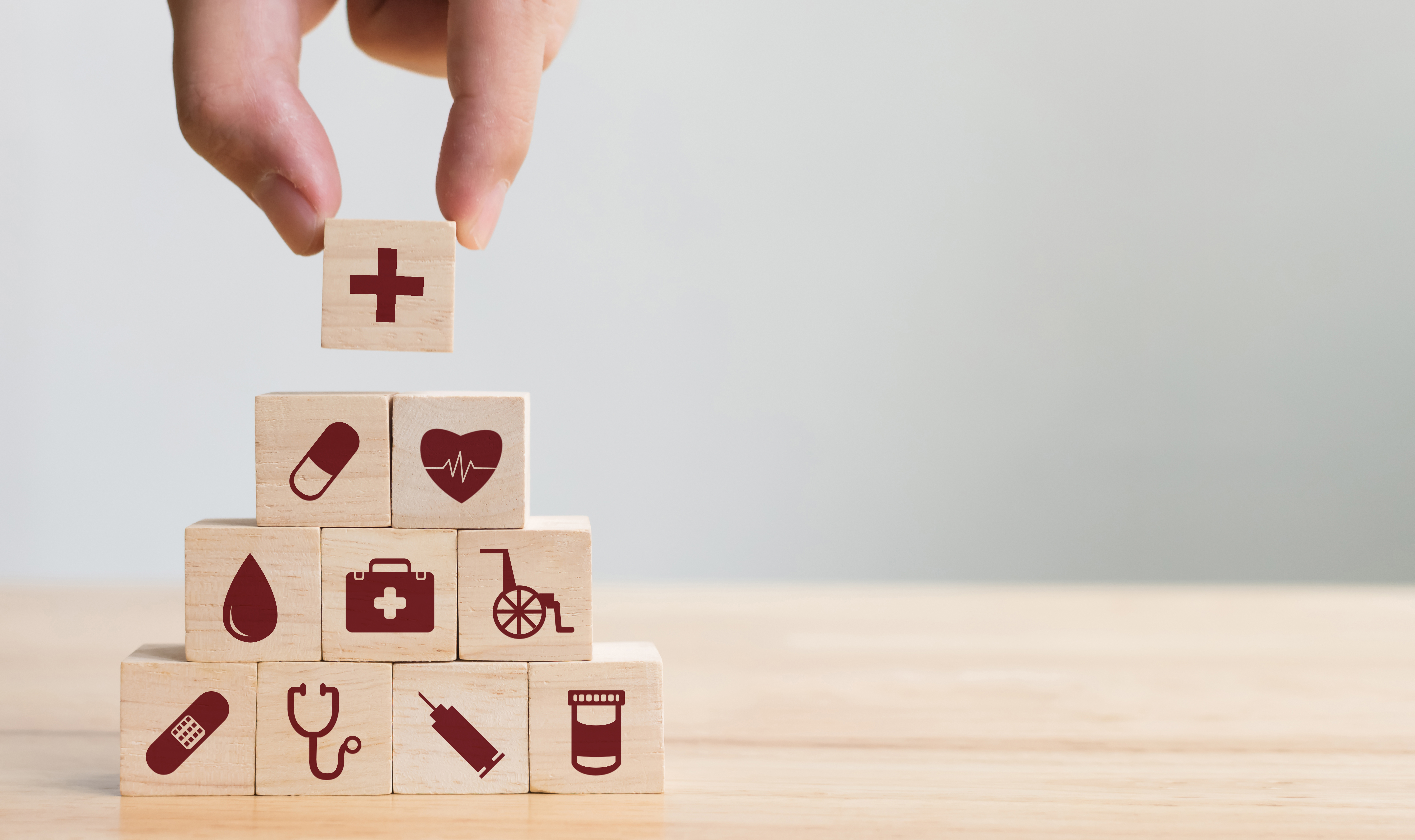 Hand placing wood toy block on top of a tower. The blocks all have images of medical-related items on them, like pills, stethoscope, syringe