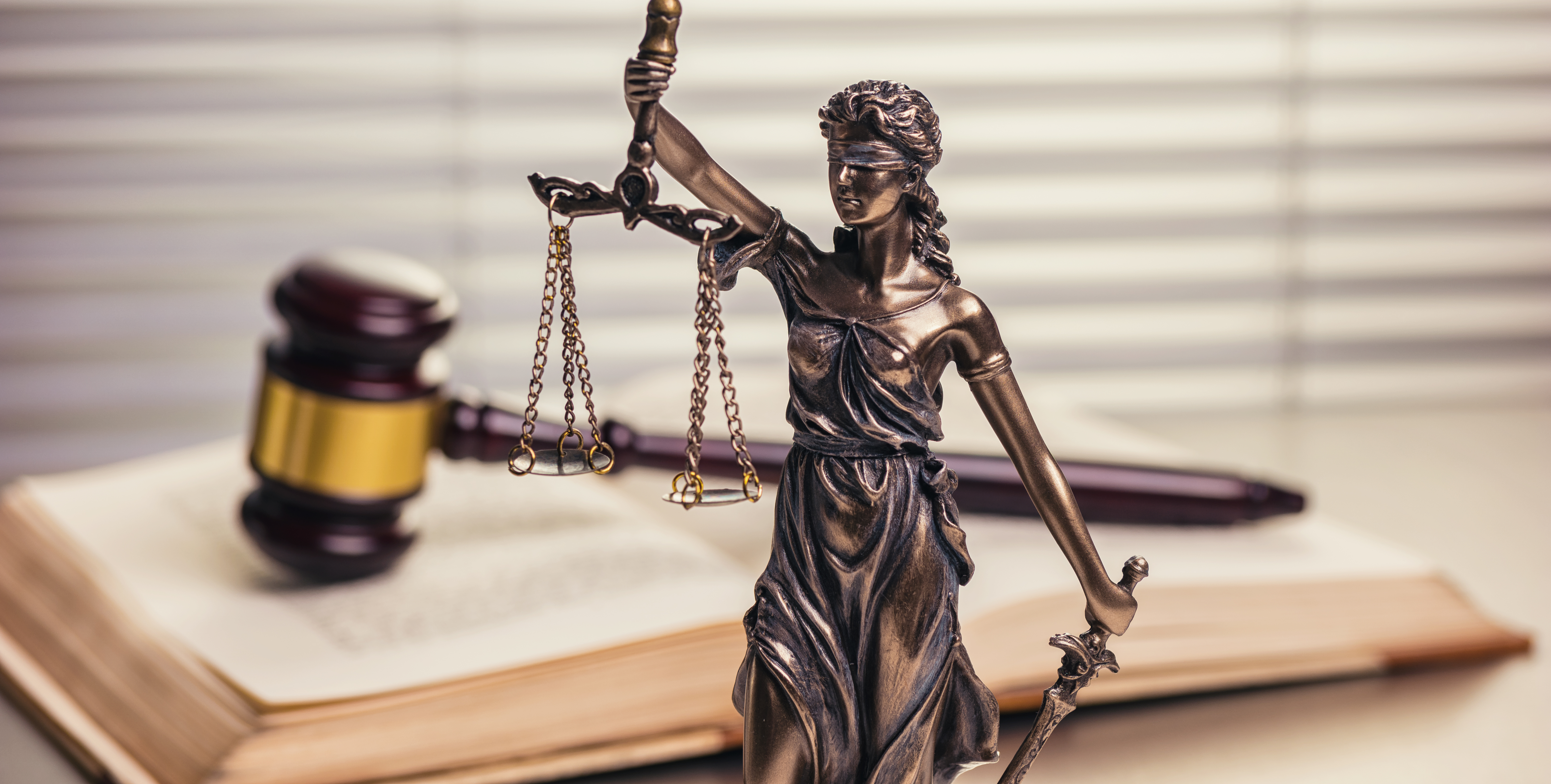 Statue of Justitia, the Roman goddess of Justice, placed in front of a large open book on which a gavel has been placed.