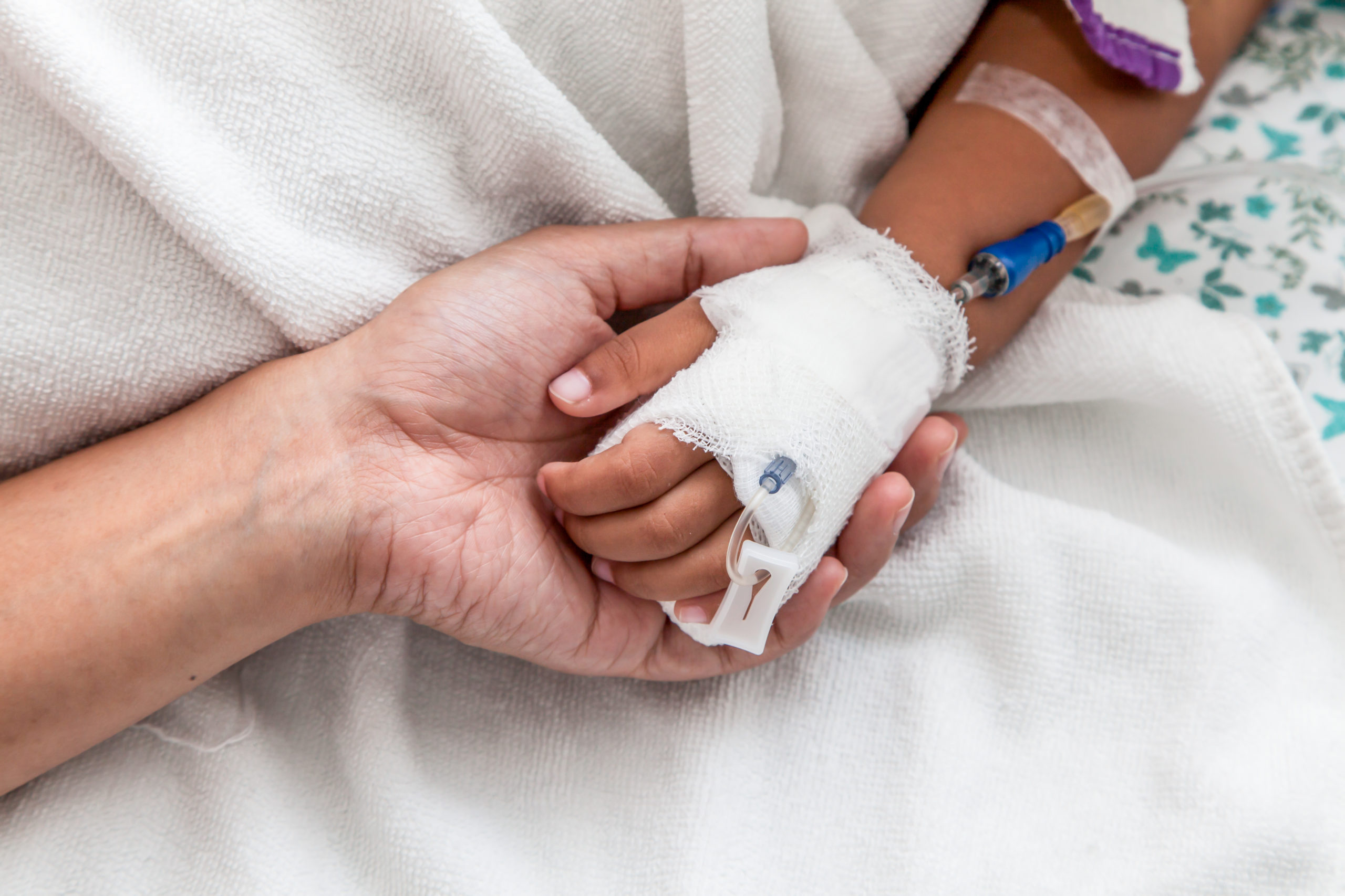 An adult hold the hand of a child with an IV