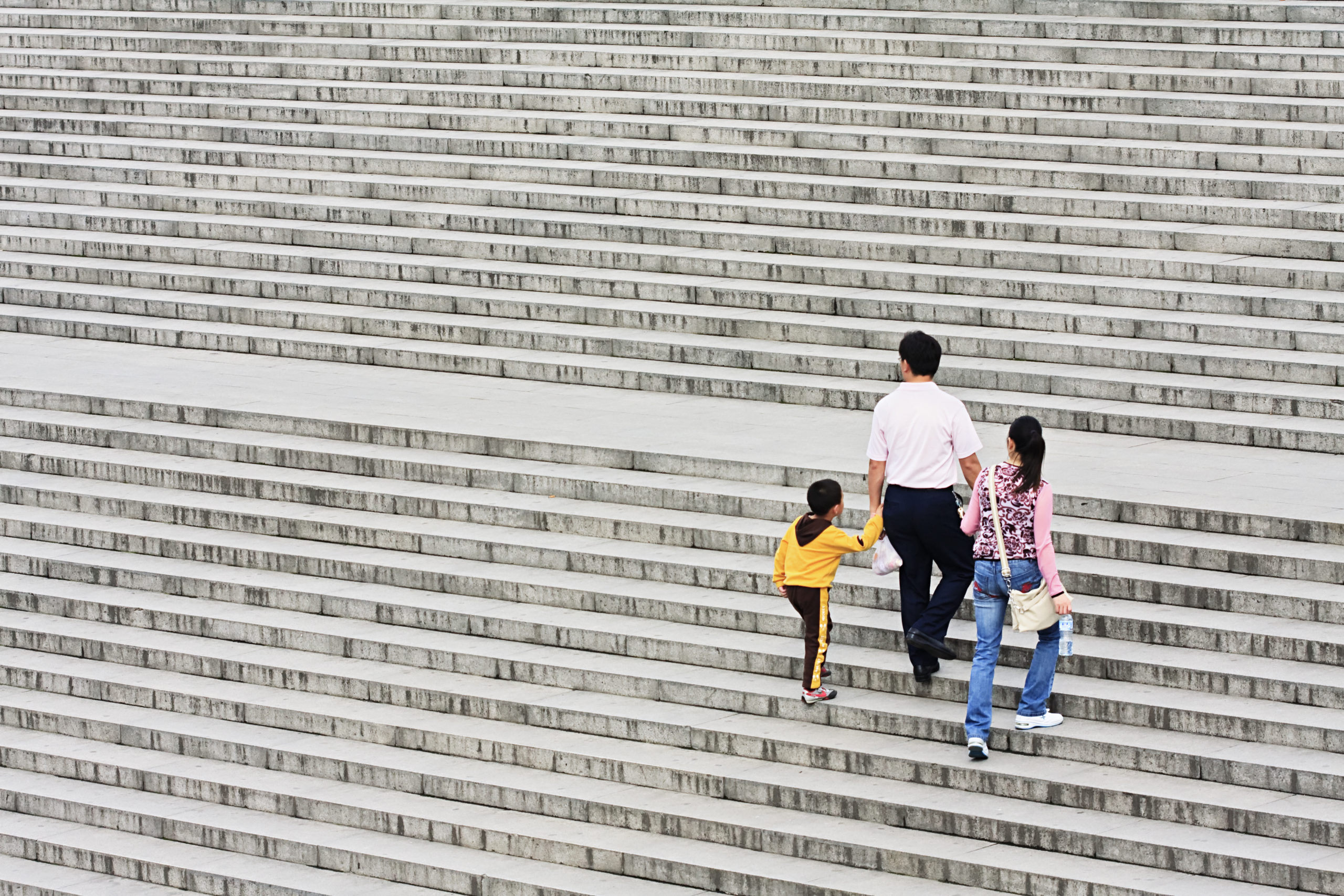 A family consisting of two adults and one child walk stairs with their backs to the camera.