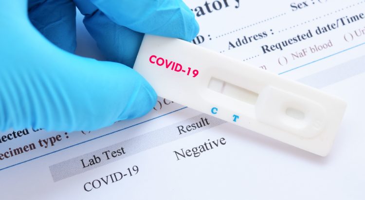 Gloved hand holding medical rapid test labeled COVID-19 over sheet of paper listing the test result as negative.