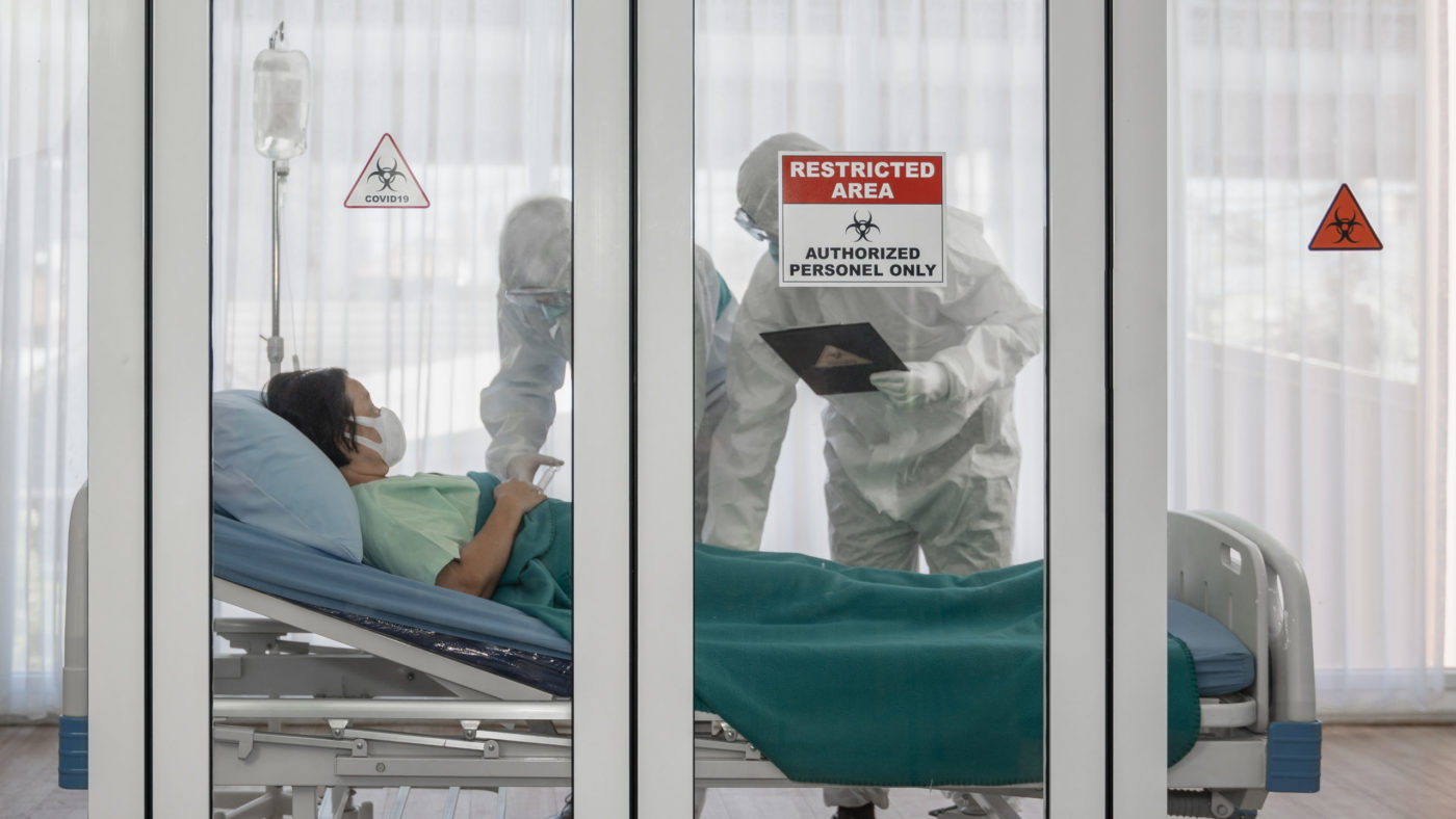 Health care workers in personal protective equipment attend to a patient.