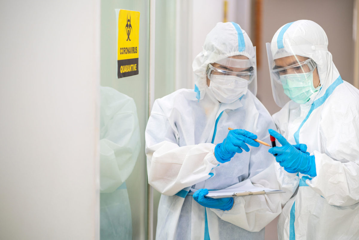 Doctors hold blood sample wearing ppe suit and face mask in hospital.