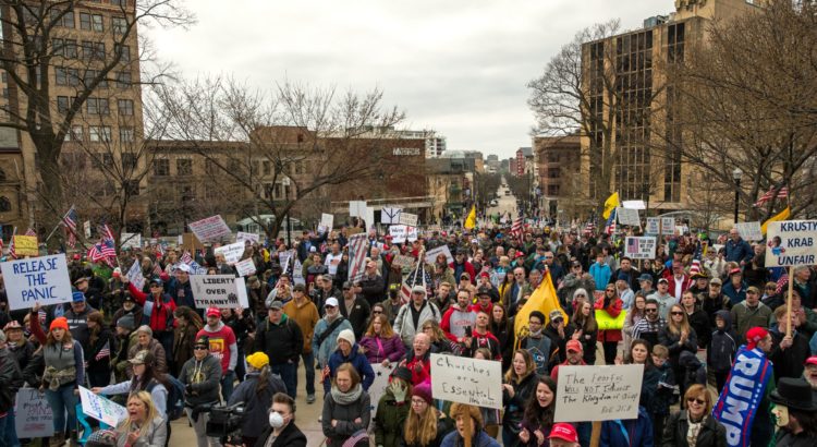 Madison, Wisconsin / USA - April 24, 2020: Demonstrators hold flags and signs at an anti lockdown rally on the steps of the Wisconsin State capitol. State Street is in the background.