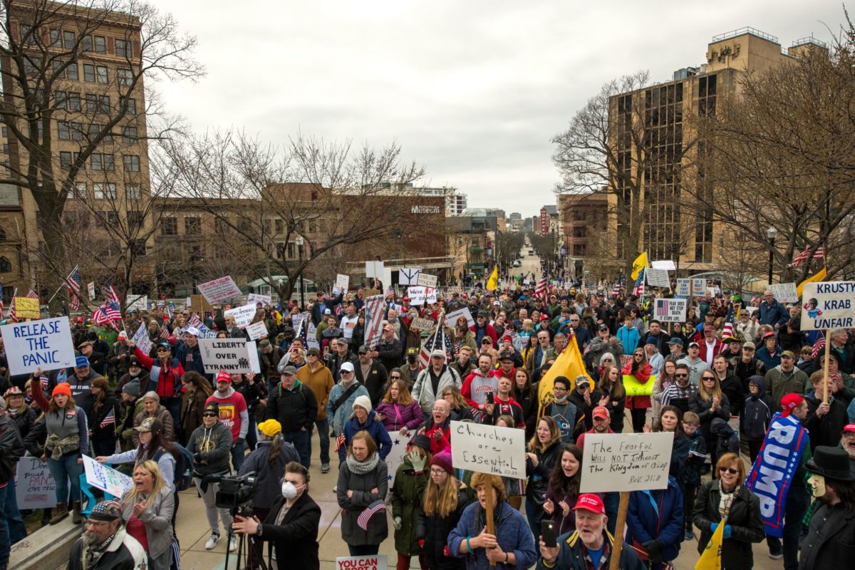 Madison, Wisconsin / USA - April 24, 2020: Demonstrators hold flags and signs at an anti lockdown rally on the steps of the Wisconsin State capitol. State Street is in the background.