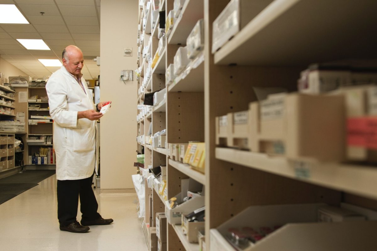 A male pharmacist is examining a drug from a pharmacy inventory.