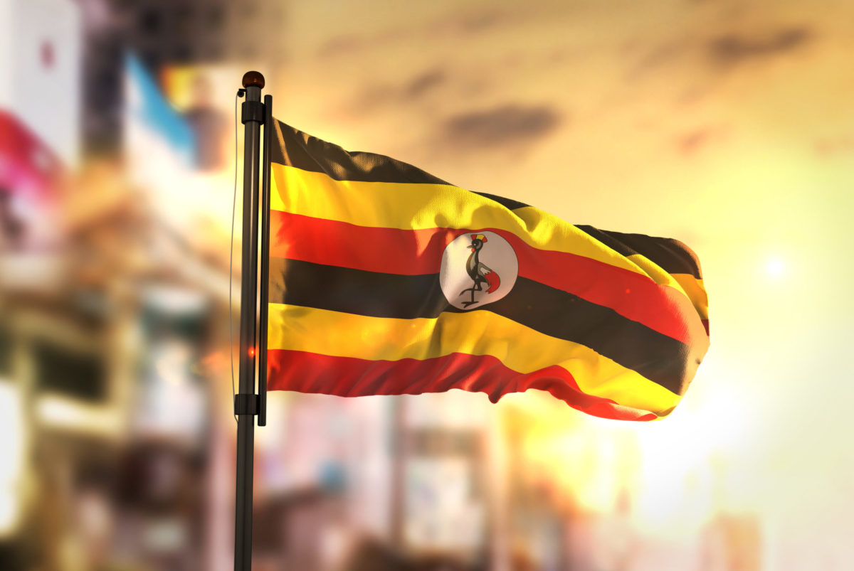 Uganda Flag Against City Blurred Background At Sunrise Backlight 3D Rendering.