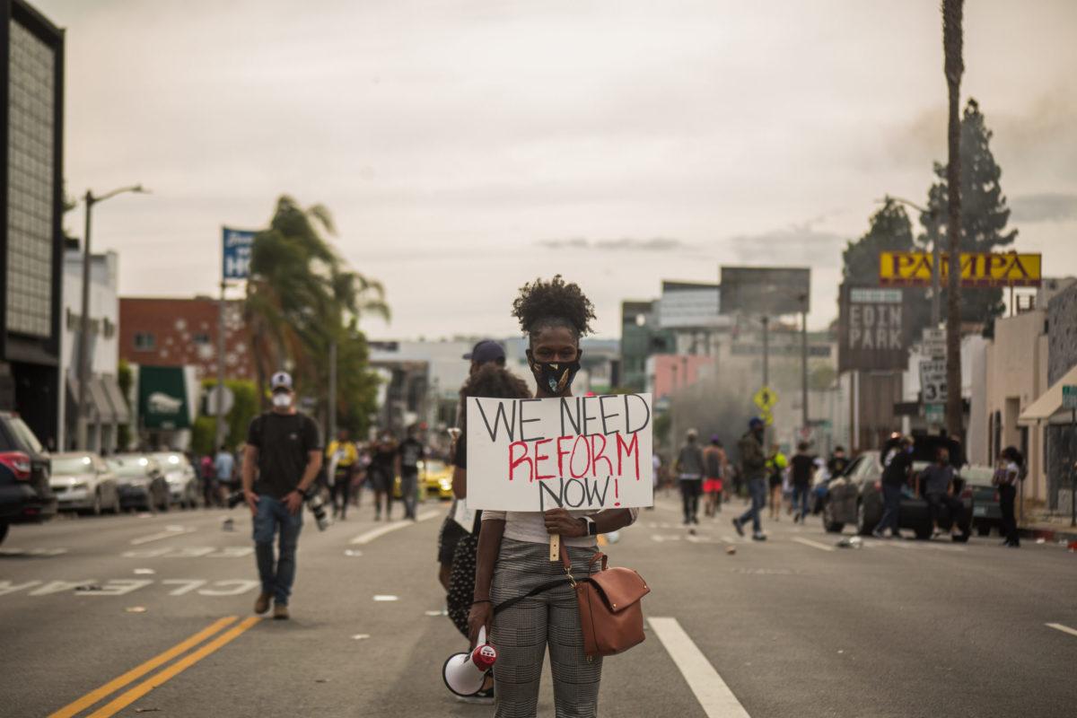 Protestor holding sign that reads: "we need reform now."