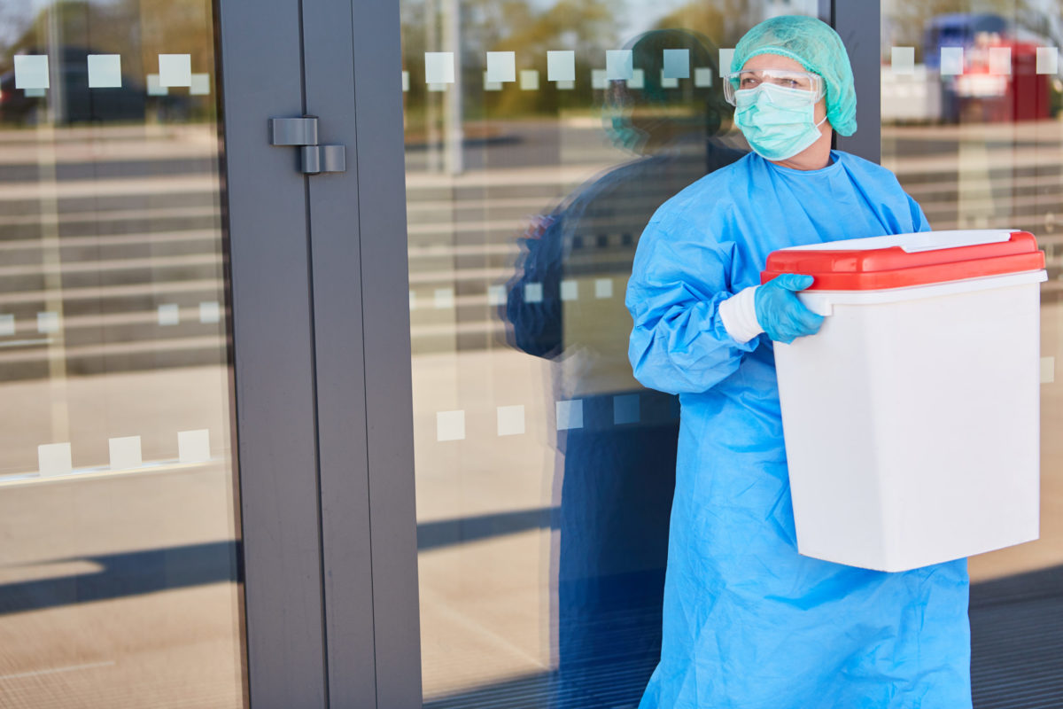 Doctor or surgeon with organ transport after organ donation for surgery in front of the clinic in protective clothing.