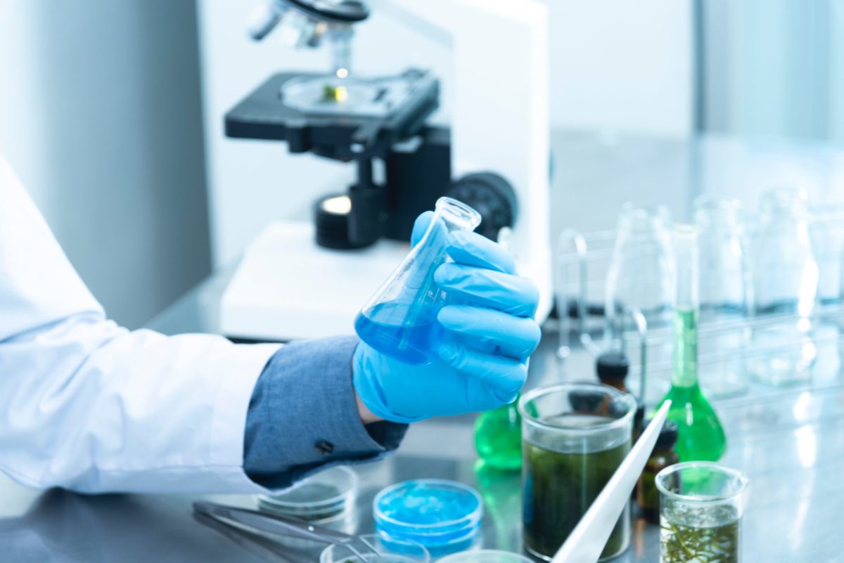 Photo of person with gloved hand holding flask at lab bench.