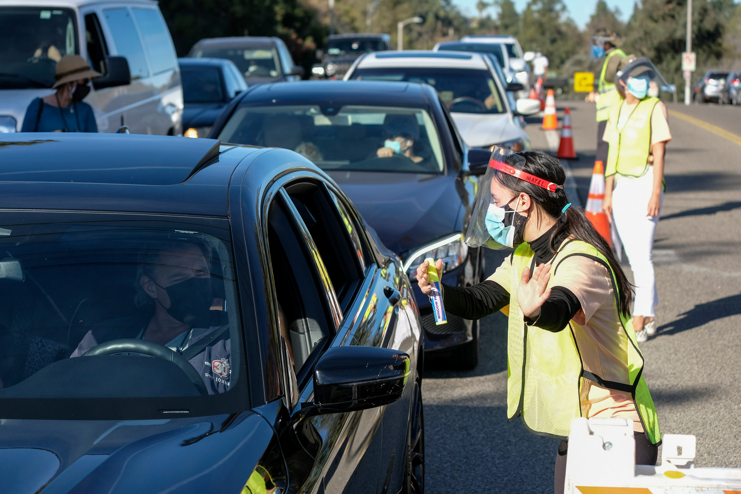 Bill of Health - A worker gives directions as motorists wait in lines to get the coronavirus (COVID-19) vaccine in a parking lot at Dodger Stadium, Friday, Jan. 15, 2021, in Los Angeles, covid vaccine distribution