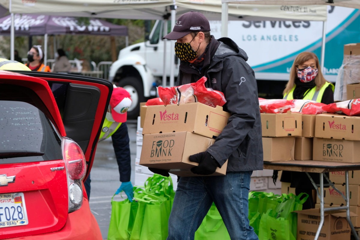 A volunteer loads food into the trunk of a vehicle during a drive thru food distribution by the Los Angeles Regional Food Bank at Exposition Park on Saturday, Jan. 23, 2021, in Los Angeles.