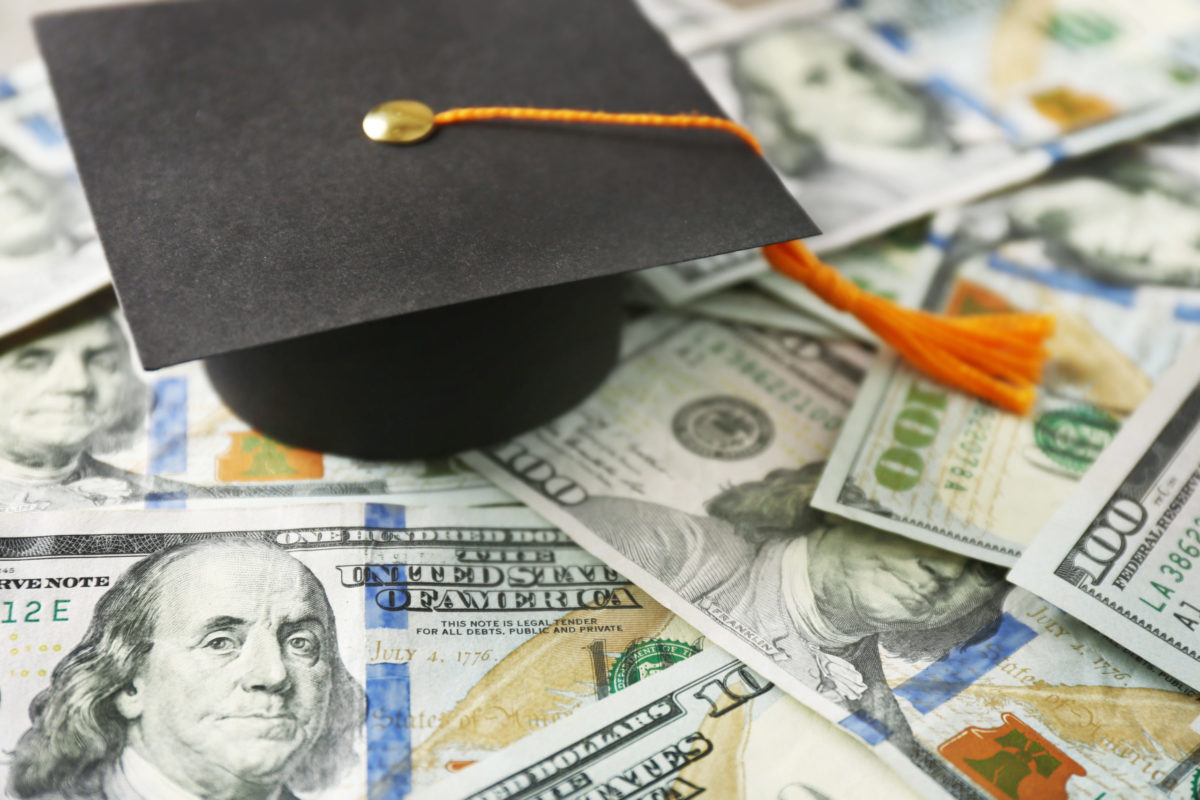 Close up view of graduation hat on dollar banknotes. Tuition fees concept.