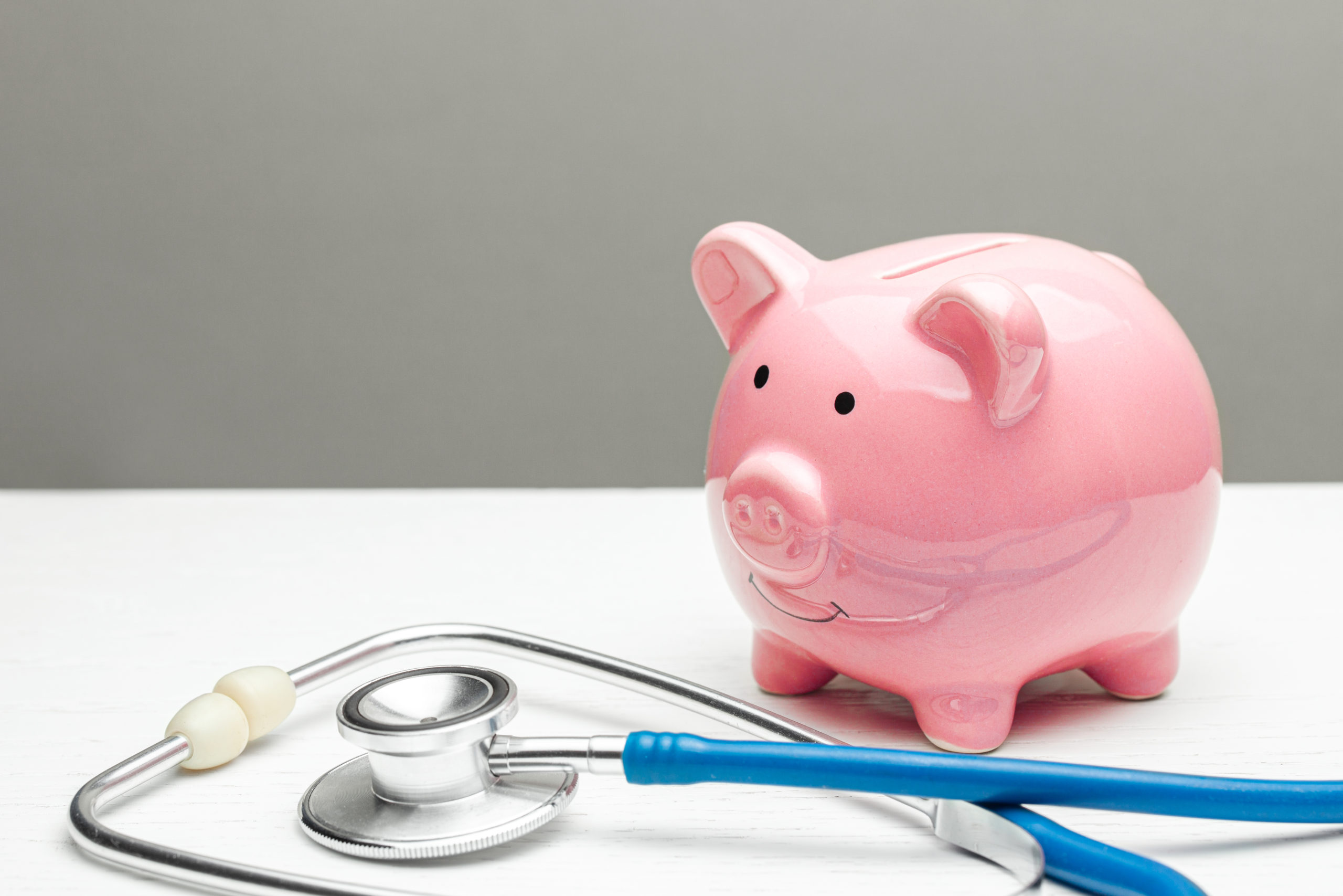 Pink piggy bank and stethoscope on a gray background.