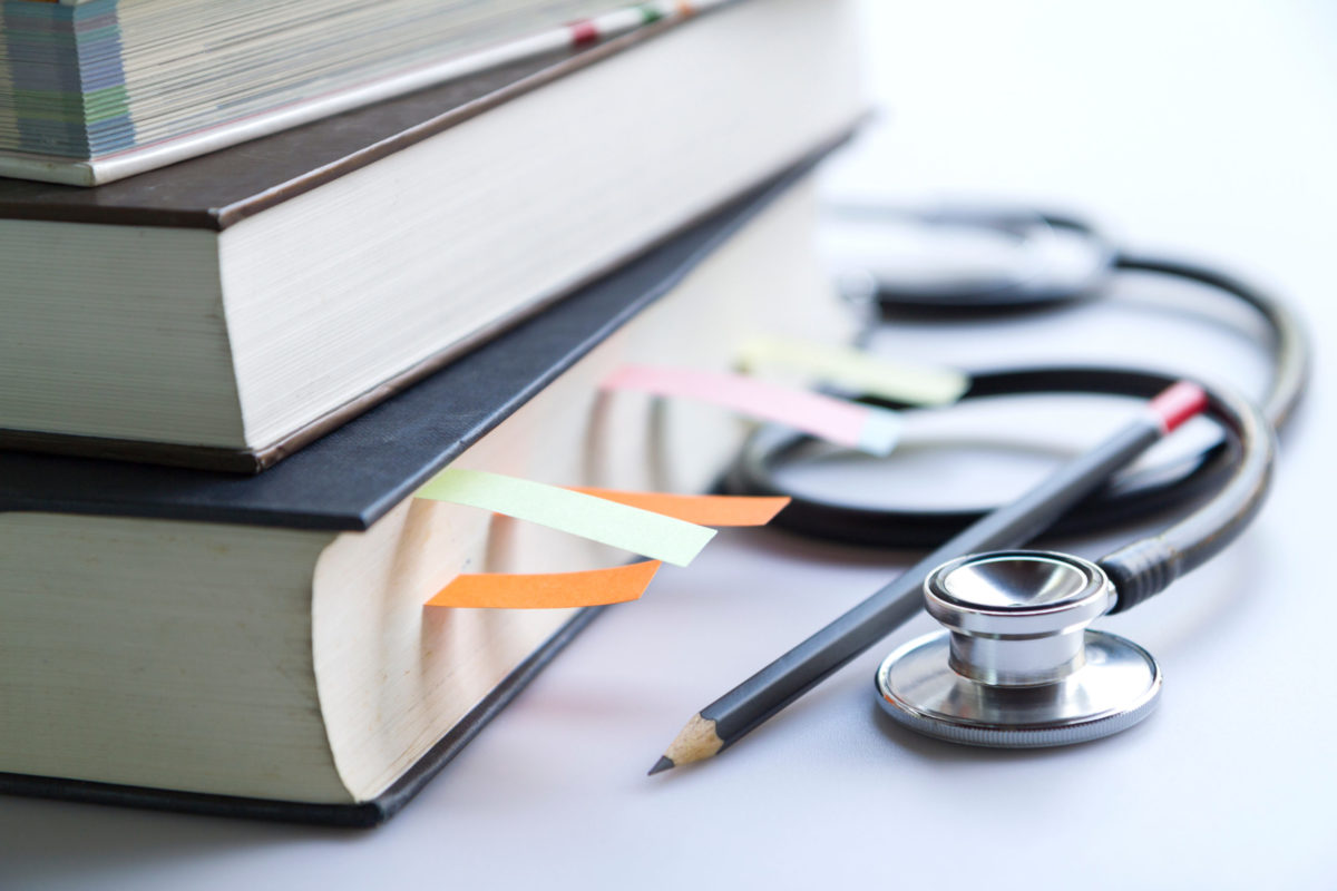 Medical student textbooks with pencil and multicolor bookmarks and stethoscope isolated on white.