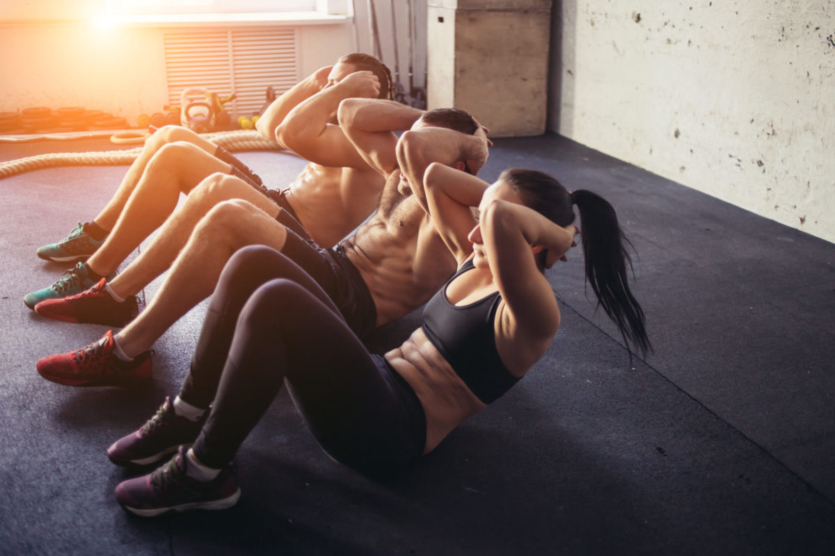 Group of athletic adult men and women performing sit up exercises to strengthen their core abdominal muscles at fitness training.