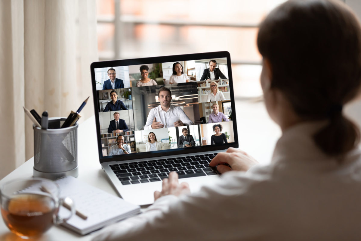 View over woman' shoulder seated at desk, videoconferencing on computer.