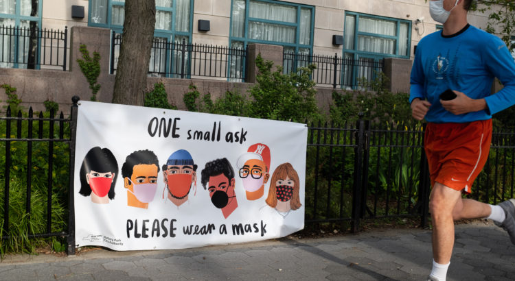 NEW YORK, NEW YORK: MAY 18, 2020: A jogger runs past a banner by the Battery Park City Authority reminding park visitors to please wear face masks.