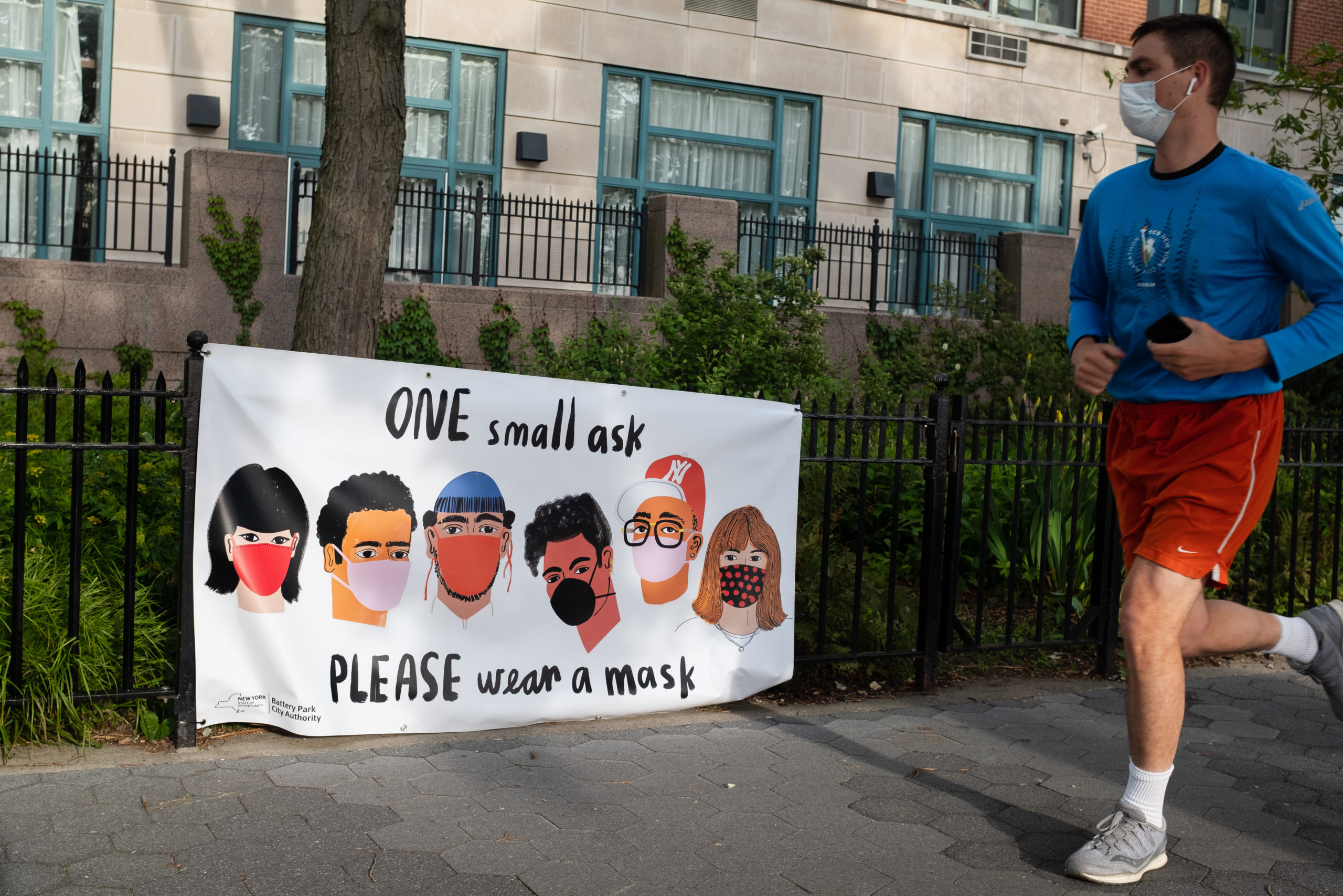 NEW YORK, NEW YORK: MAY 18, 2020: A jogger runs past a banner by the Battery Park City Authority reminding park visitors to please wear face masks.