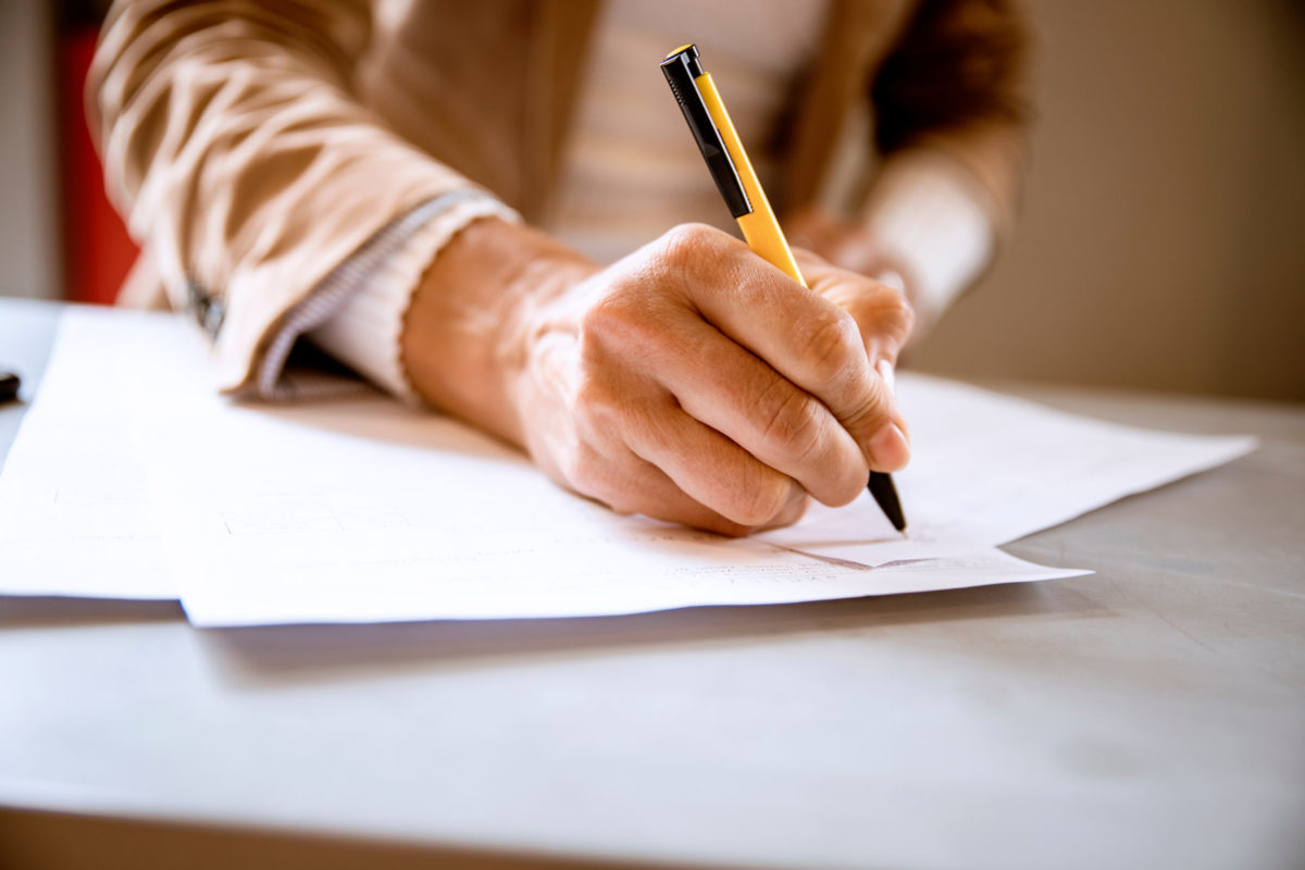 Female hand writing signature on the paper document.