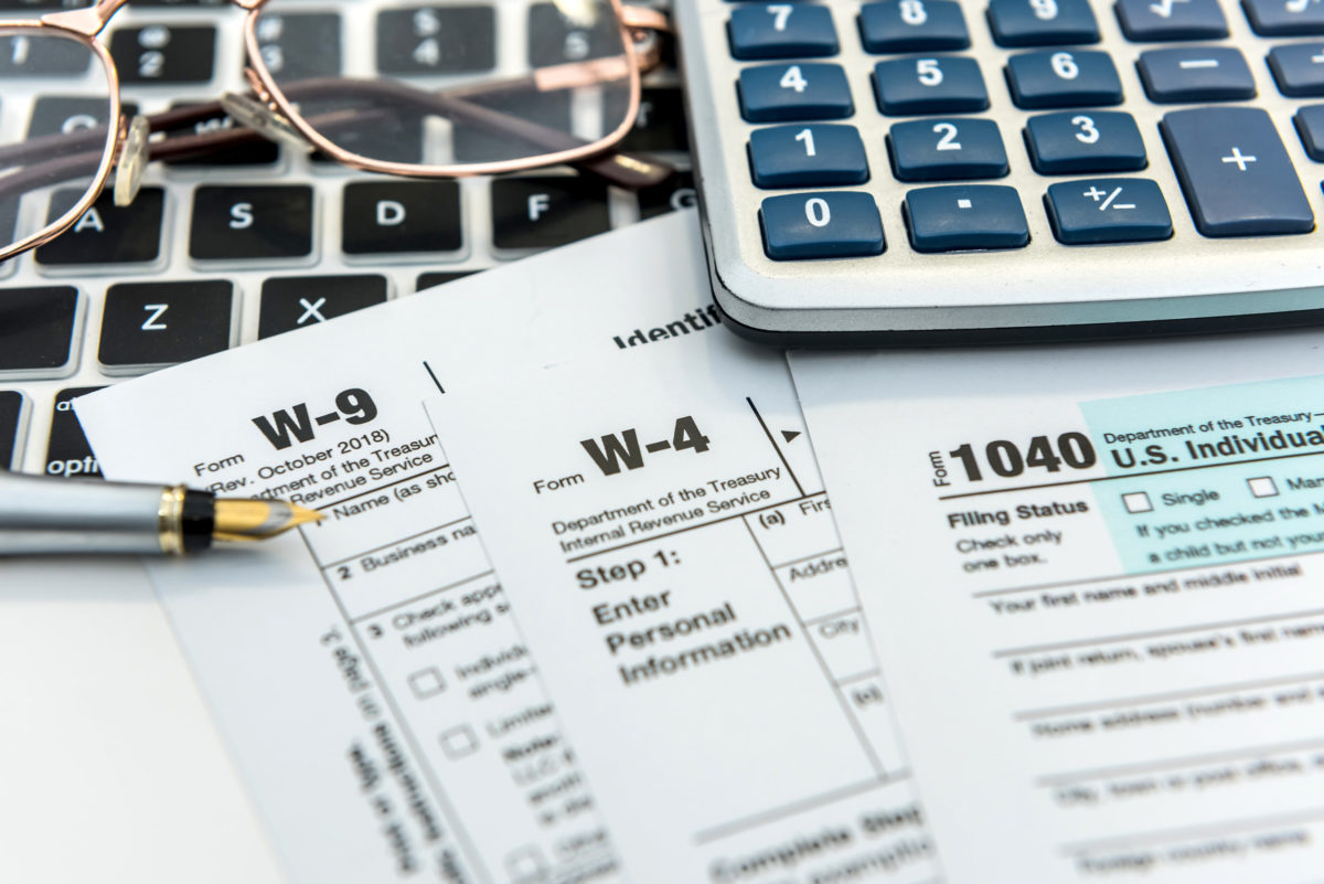 Tax forms with laptop, glasses, pen, and calculator.