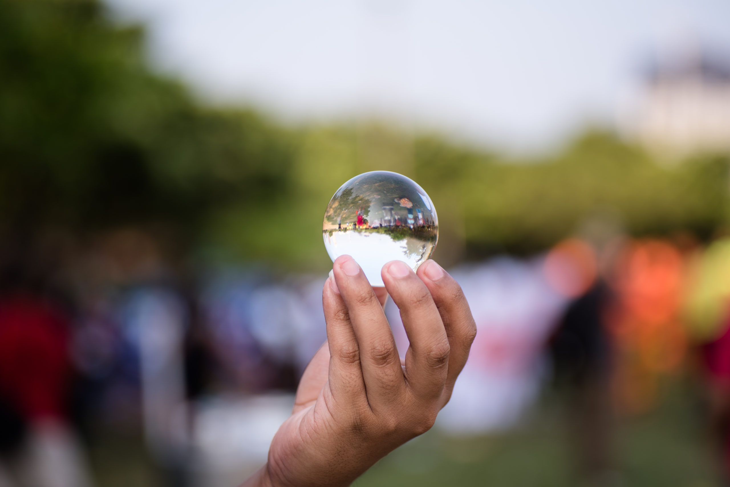 Hand holding glass ball with inverted image of surroundings reflected in ball.