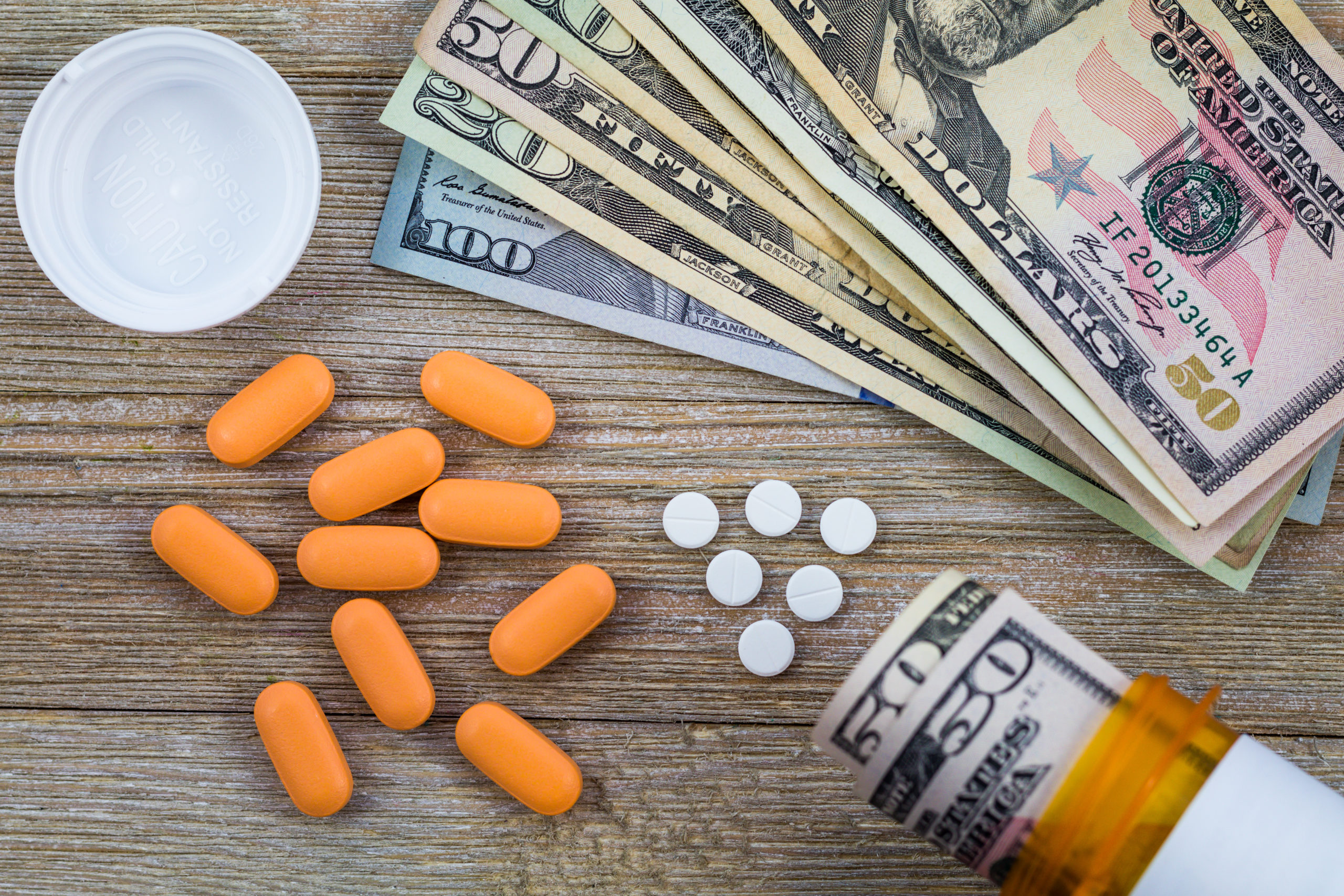 Bill of Health - American currency (50, 100, 20) on a wooden table next to pills and spilling bottle of pharmaceuticals