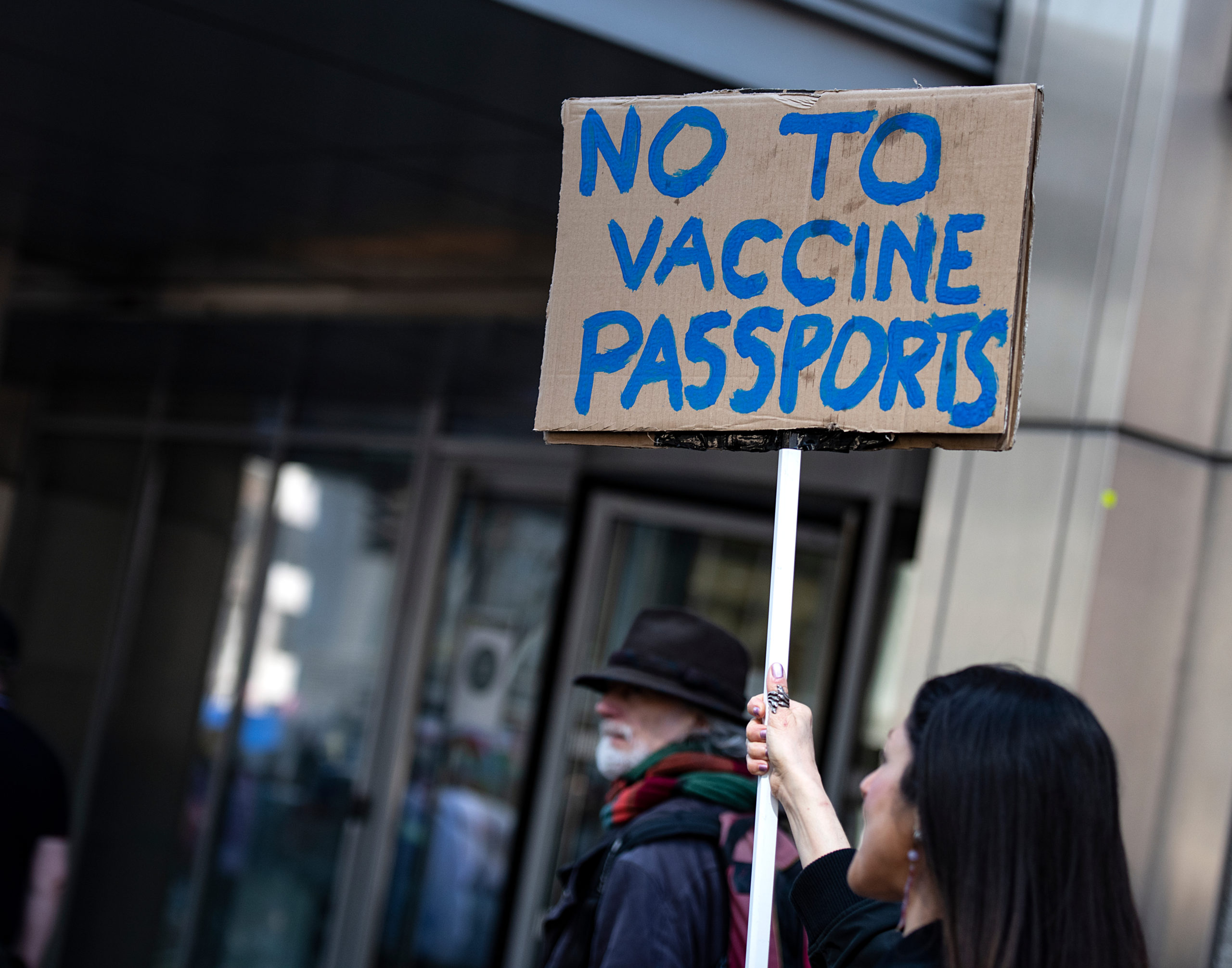 Bill of Health - women holds carboard protest sign reading "no to vaccine passports," vaccine passports legality