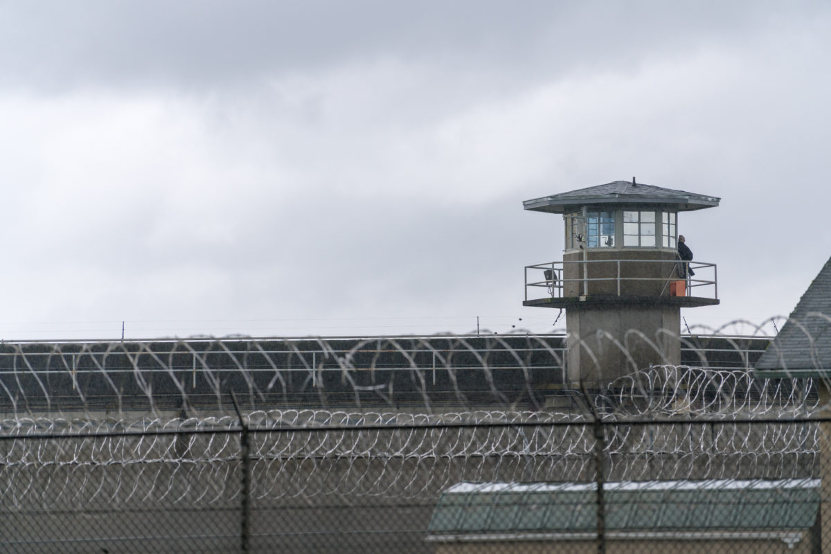 An armed guard surveys the grounds from the railing of a prison watchtower.