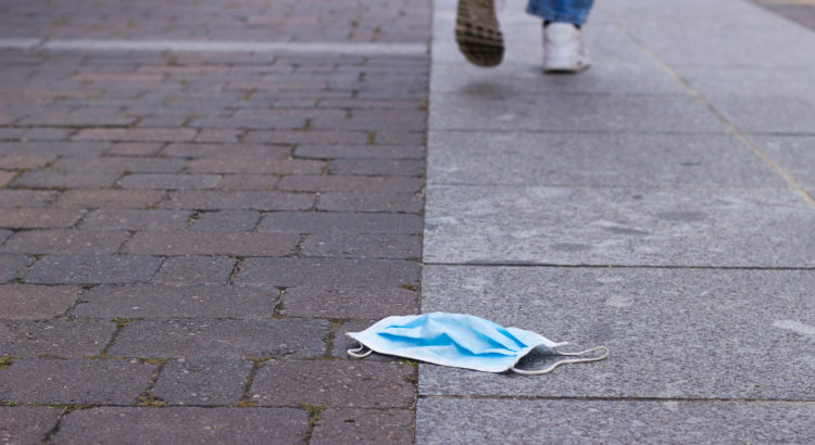 person walking away from a surgical mask lying on the ground.