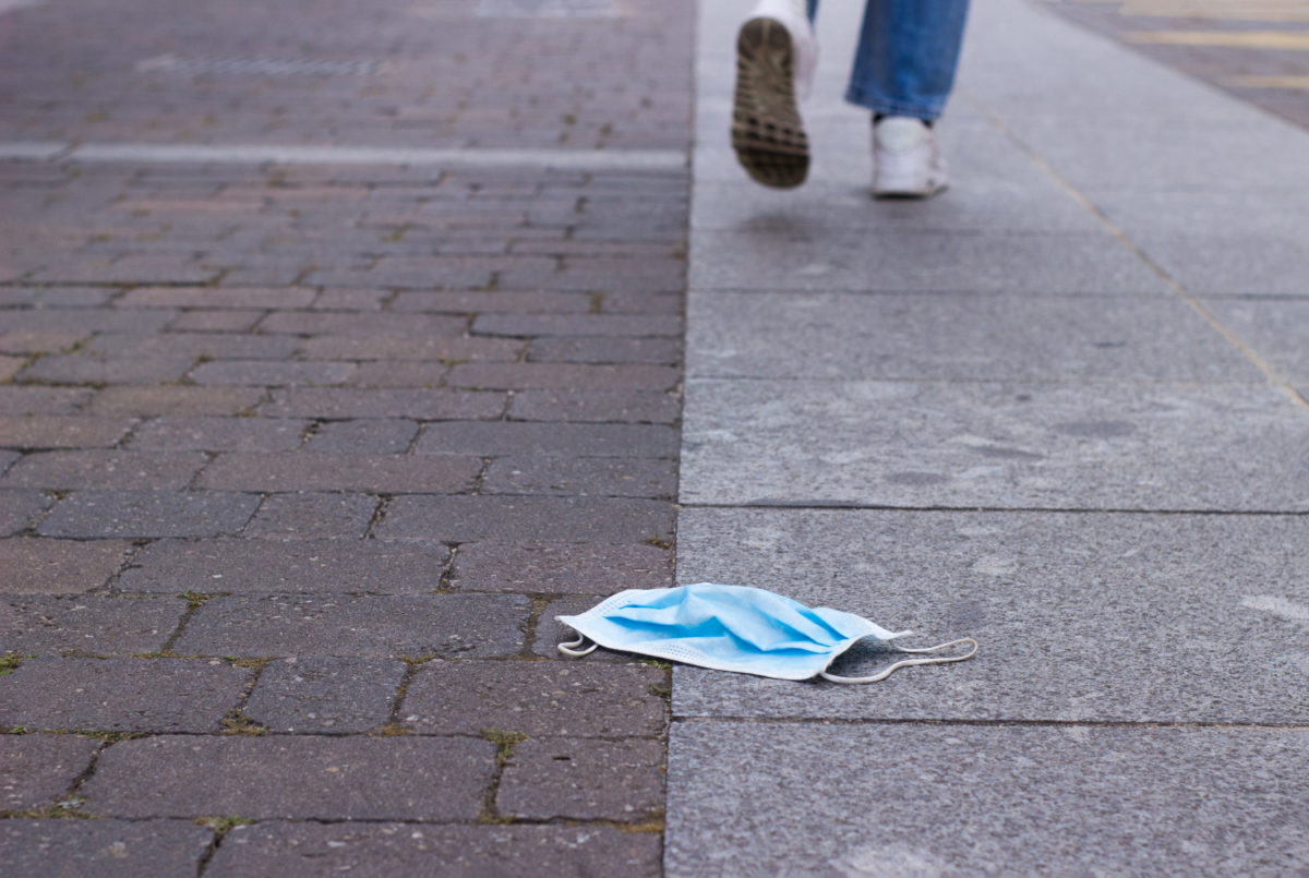 person walking away from a surgical mask lying on the ground.