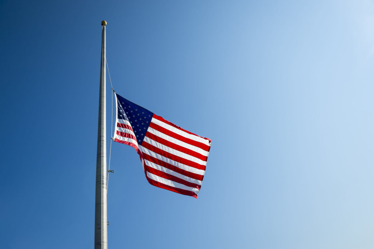 American flag lowered to half mast in bright blue sky.