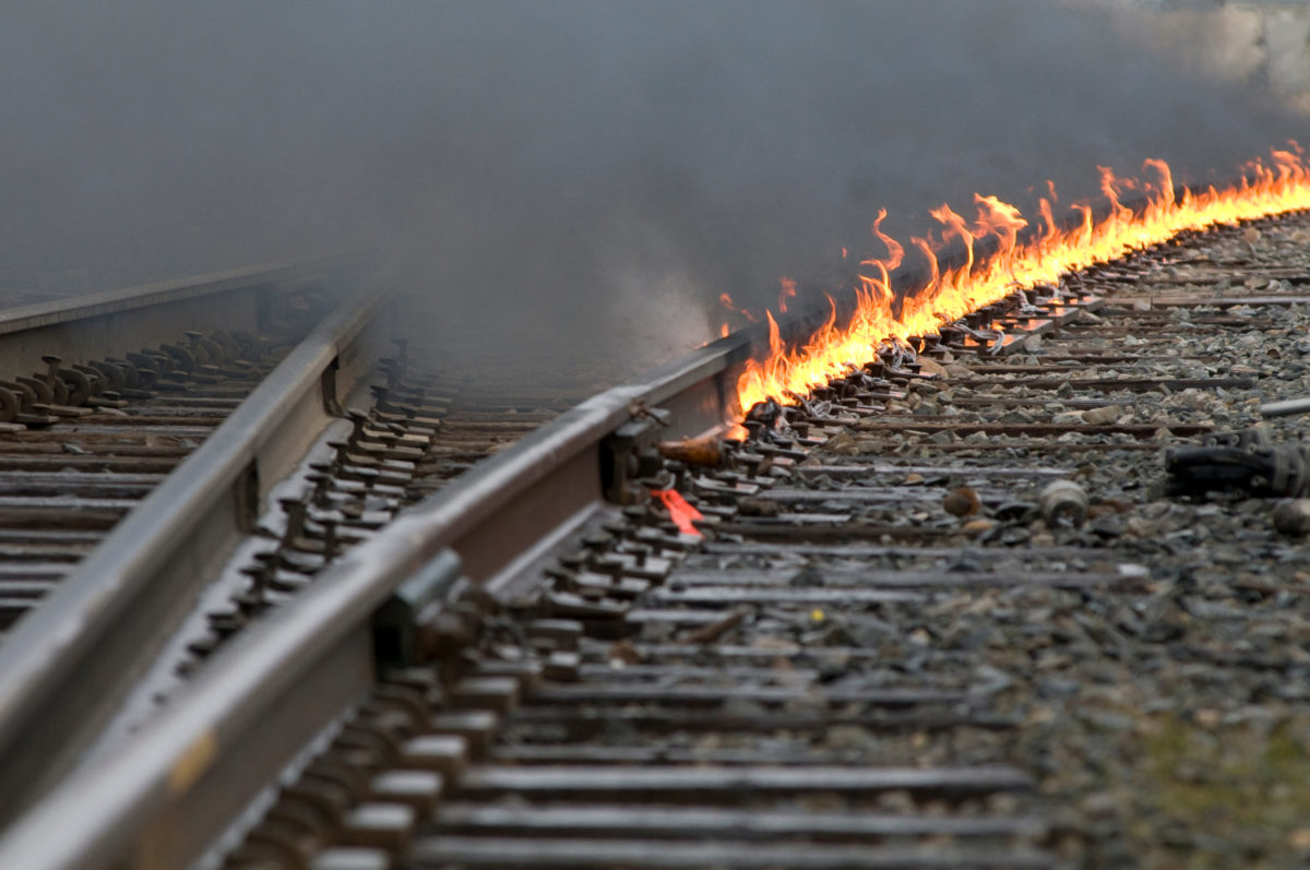 Train tracks interchange leading around a curve as a controlled fire burns on the track during repairs.