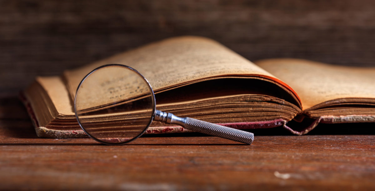 Vintage history book and magnifying glass on wooden background.