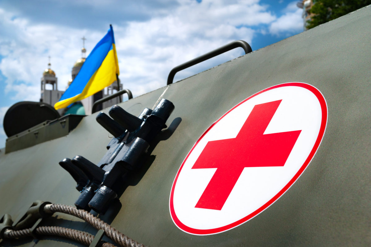 Medical armored personnel carrier. Medical cross on the armor of an armored vehicle against the background of the flag of Ukraine at exhibition ARMS AND SECURITY - 2021. Kiev. Ukraine - June 18, 2021.