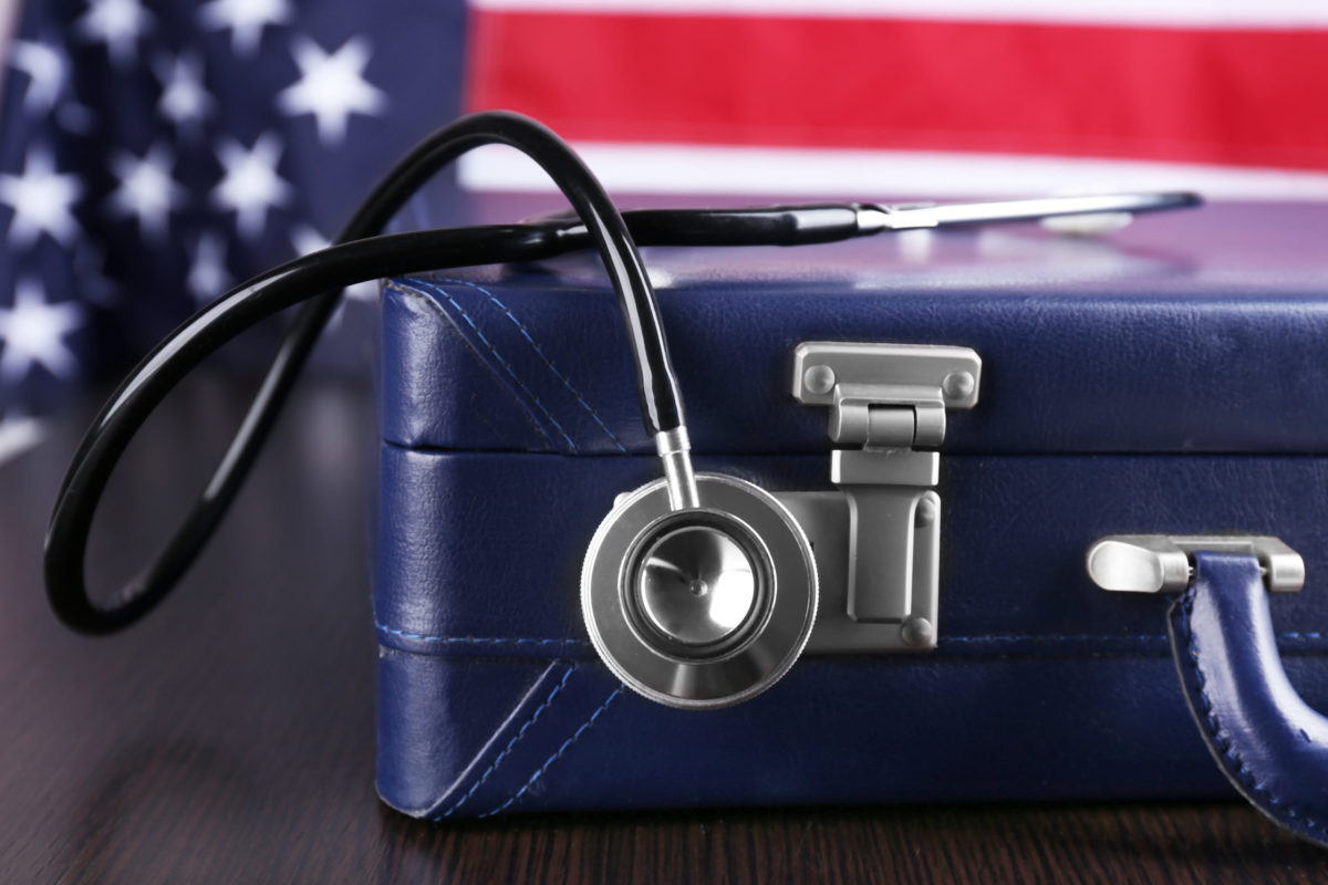 Stethoscope with blue suitcase on a table with American flag as background.