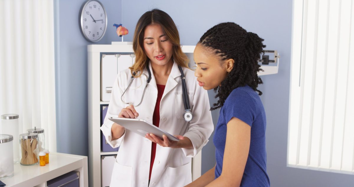 African American patient explaining issues to Asian doctor using tablet.