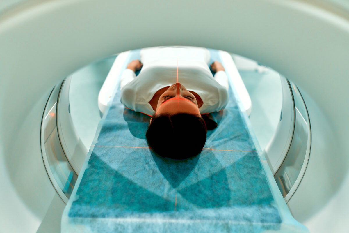 Portrait of a patient lying on CT or MRI, the bed moves inside the machine, scanning her body and brain.