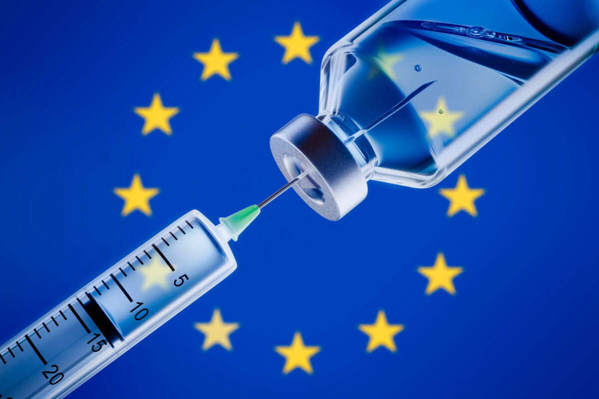 Vaccine and syringe in front of EU flag.